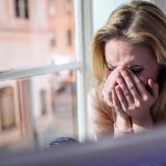 Woman sitting on windowsill, looking out of window, crying